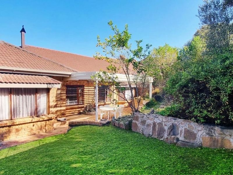 Rear view of a brick house featuring a covered patio, stone retaining wall, and a well-maintained garden area.