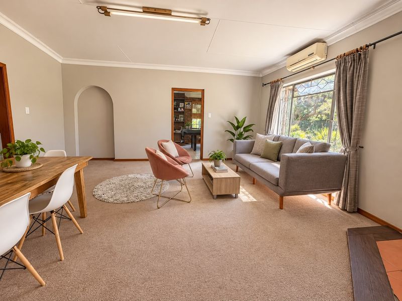 Spacious open-plan living and dining area featuring neutral walls, carpeted flooring, an air conditioning unit, and a charming arched doorway.