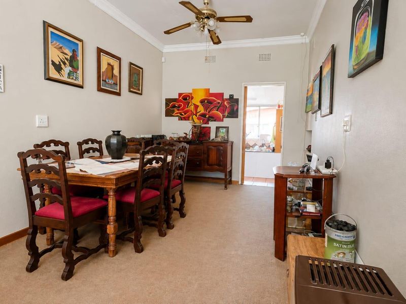 A dining room featuring a ceiling fan, crown molding, and a brick fireplace, with a doorway leading to an adjacent space.
