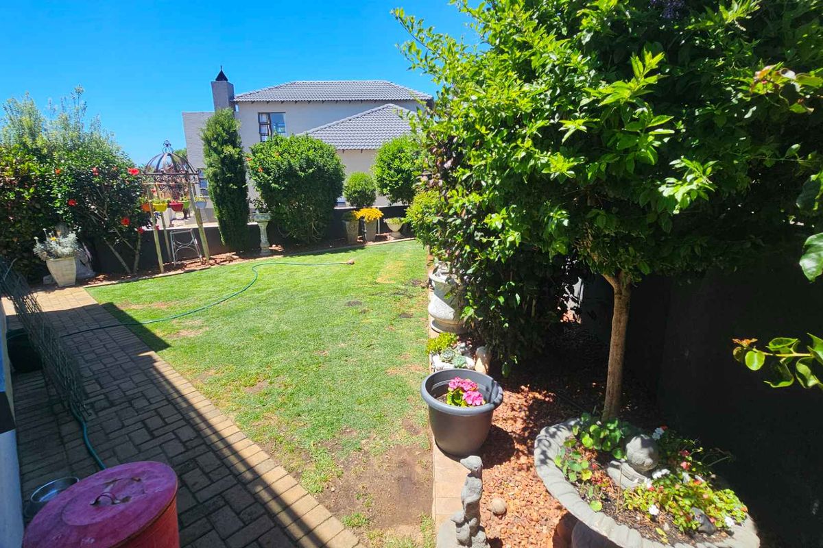 A well-maintained rear garden featuring a paved walkway, manicured lawn, and established perimeter landscaping with mature shrubs and trees.