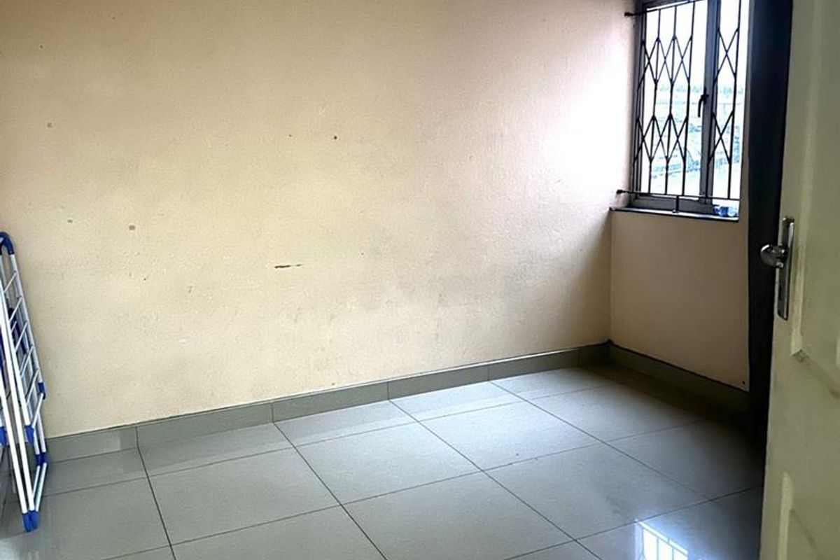 A vacant bedroom featuring neutral tiled flooring, a window with security bars, and plain painted walls.