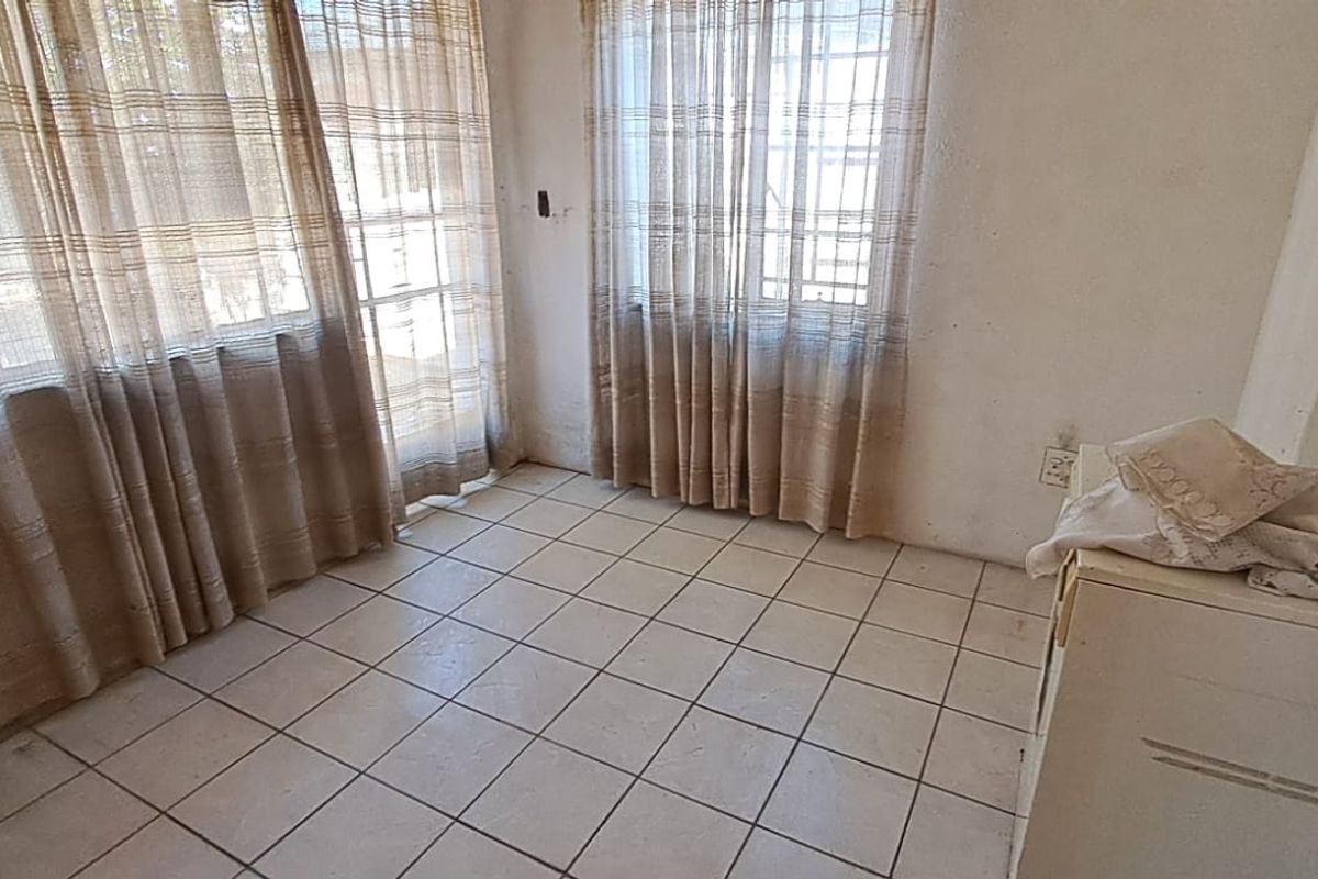 A vacant living area featuring tiled flooring, large windows with security bars, and a sliding glass door leading to the exterior.