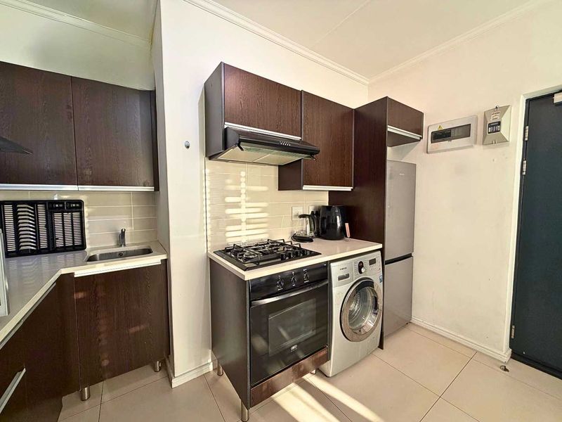 Compact kitchen featuring dark wood cabinetry, gas hob, built-in oven, extractor fan, and tiled backsplash with integrated laundry and refrigeration space.