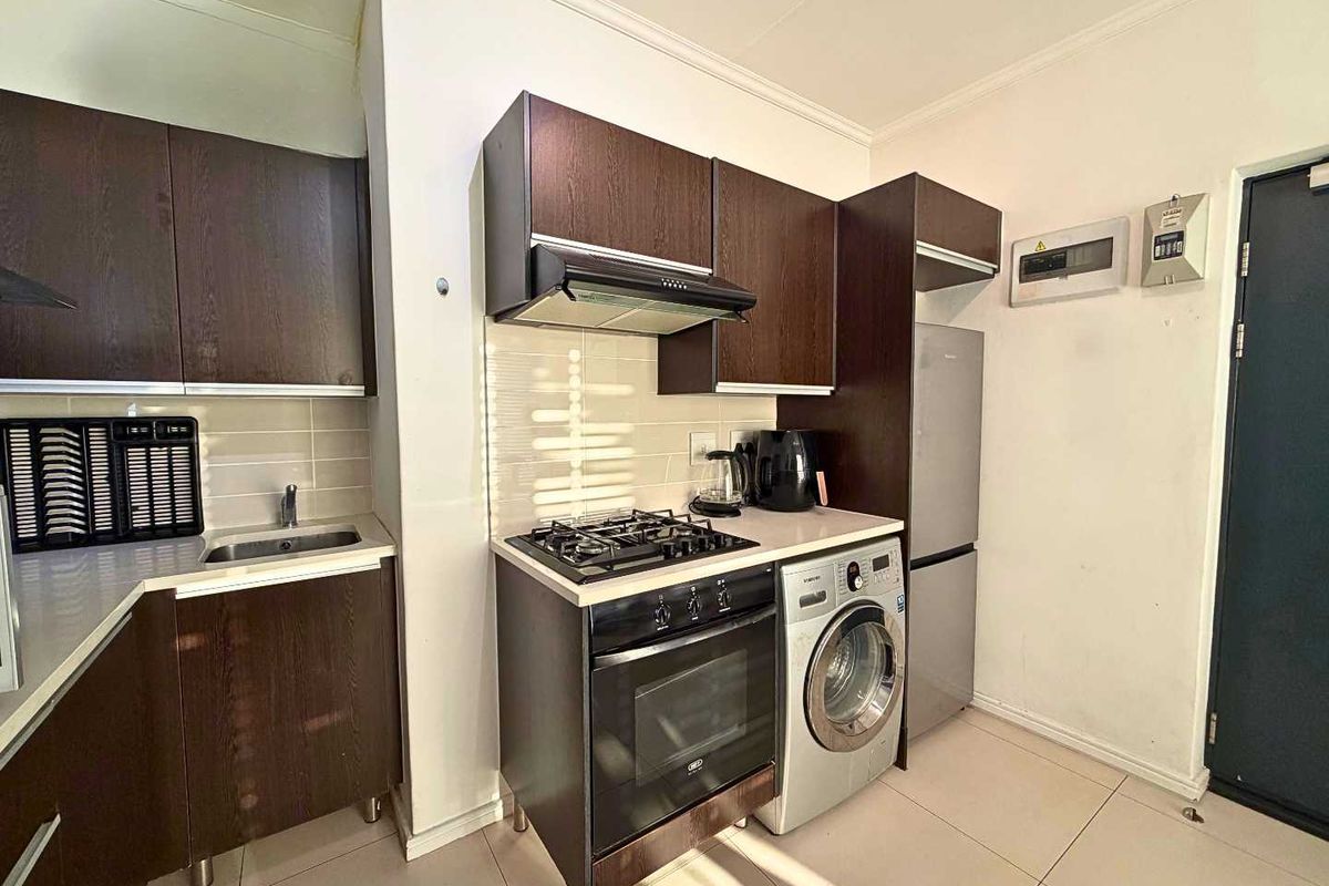 Compact kitchen featuring dark wood cabinetry, gas hob, built-in oven, extractor fan, and tiled backsplash with integrated laundry and refrigeration space.