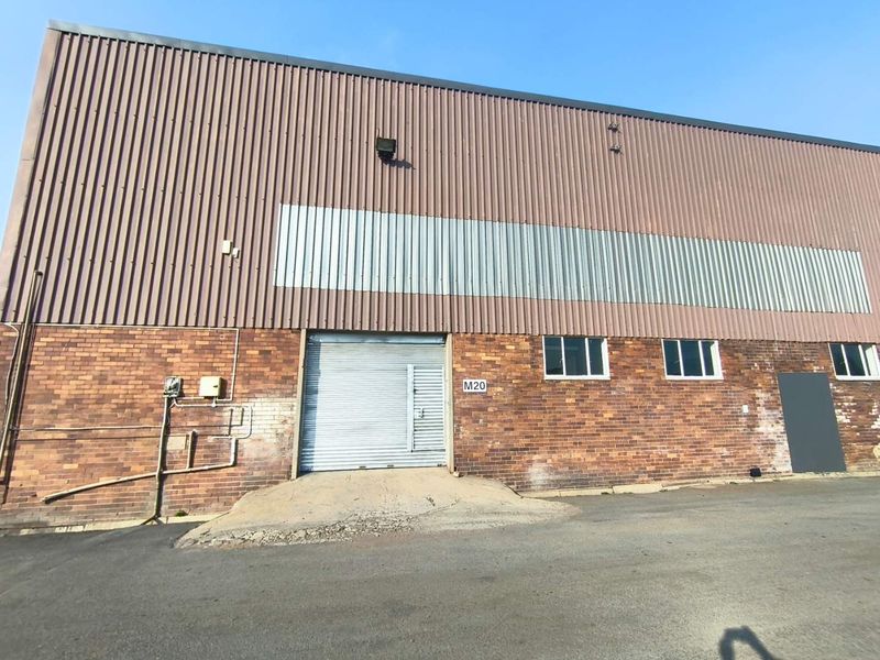 Industrial warehouse exterior featuring a brick facade, corrugated metal cladding, and a roller shutter door with a concrete loading ramp.