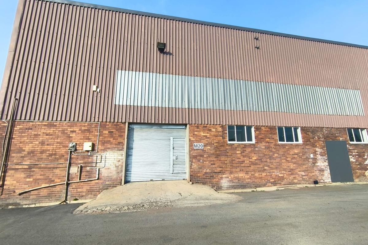 Industrial warehouse exterior featuring a brick facade, corrugated metal cladding, and a roller shutter door with a concrete loading ramp.