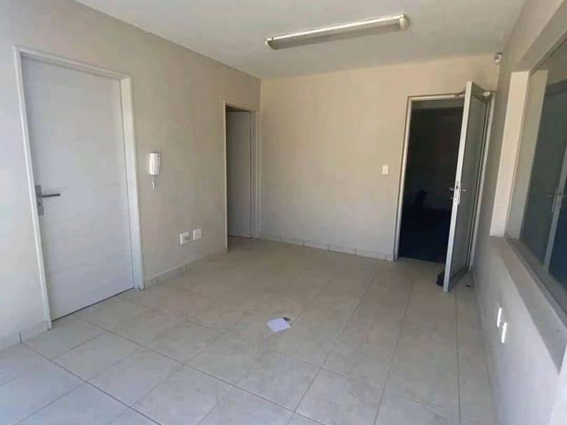 A vacant, neutral-toned office space featuring tiled flooring, multiple doorways, and functional overhead fluorescent lighting.