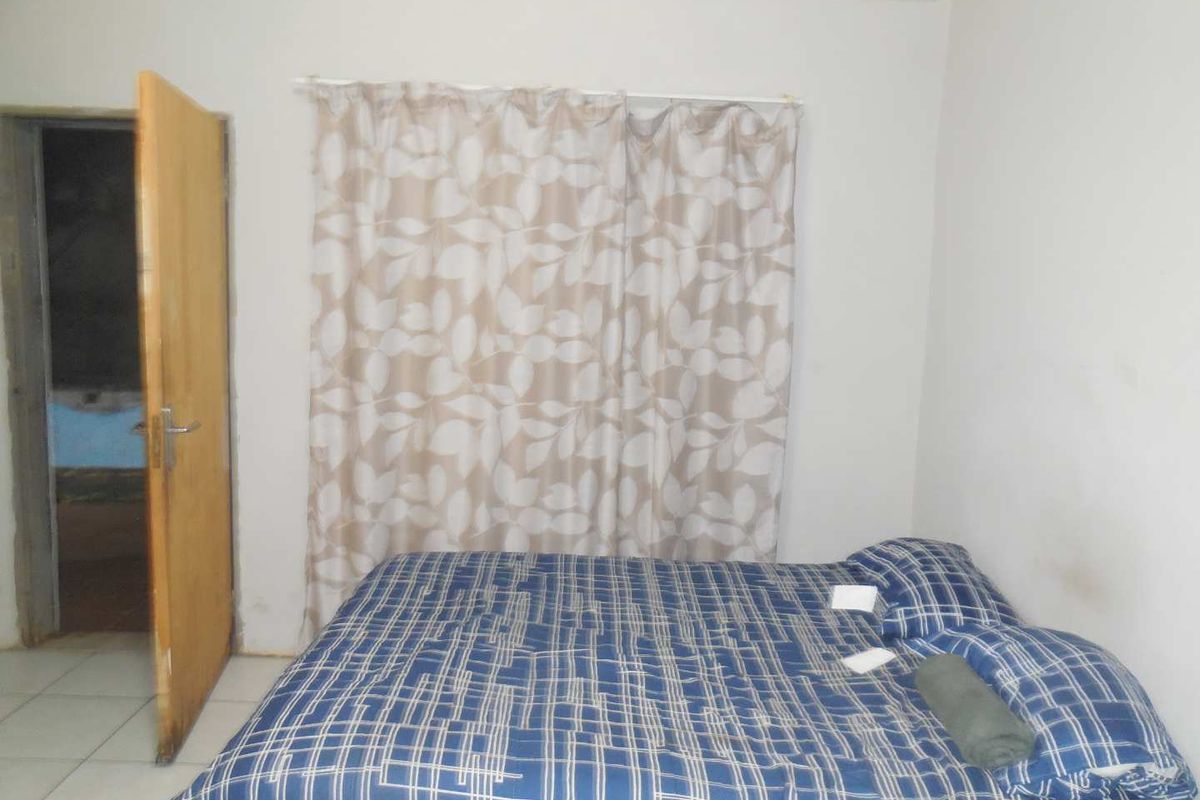 A simple bedroom featuring tiled flooring and a wooden door, requiring cosmetic updates to improve the overall aesthetic and condition.