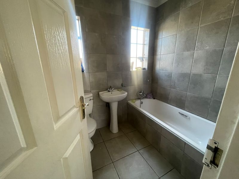 A functional bathroom featuring a pedestal sink, bathtub, and toilet with neutral grey wall and floor tiling.