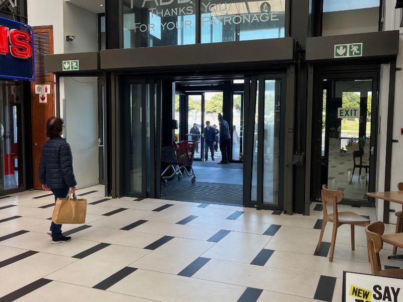 Main entrance area of the retail property featuring modern tiled flooring, large sliding glass doors, and prominent structural steel framing.