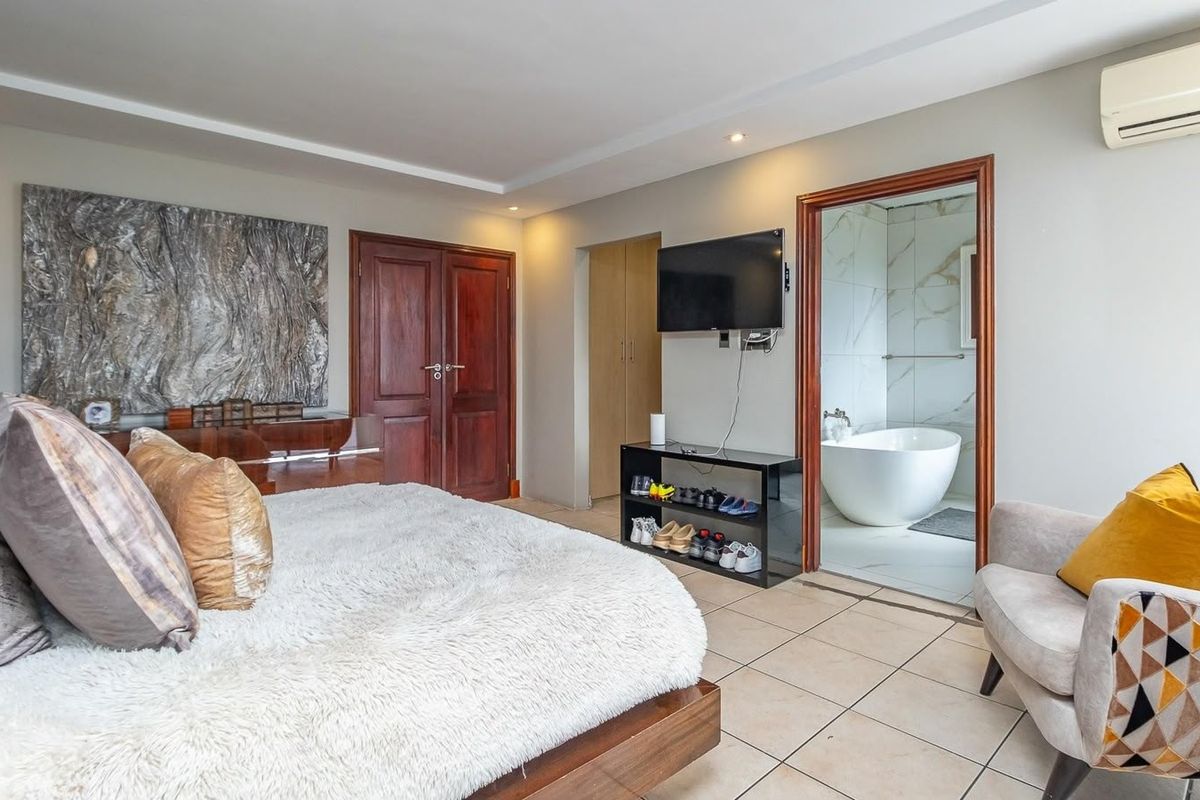 Spacious bedroom featuring tiled flooring, an air conditioning unit, built-in cupboards, and direct access to a modern en-suite bathroom with a freestanding bathtub.