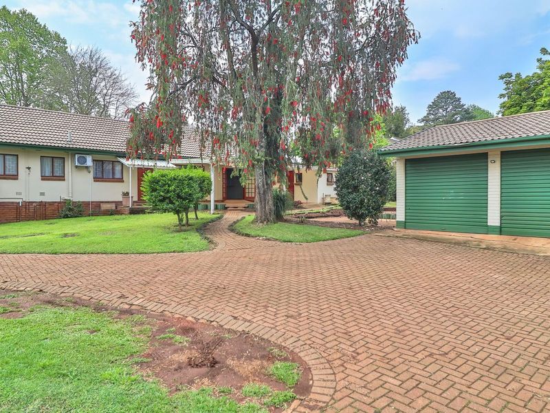 Front view of the property featuring a brick paved driveway, established garden, and a double garage with green roller doors.