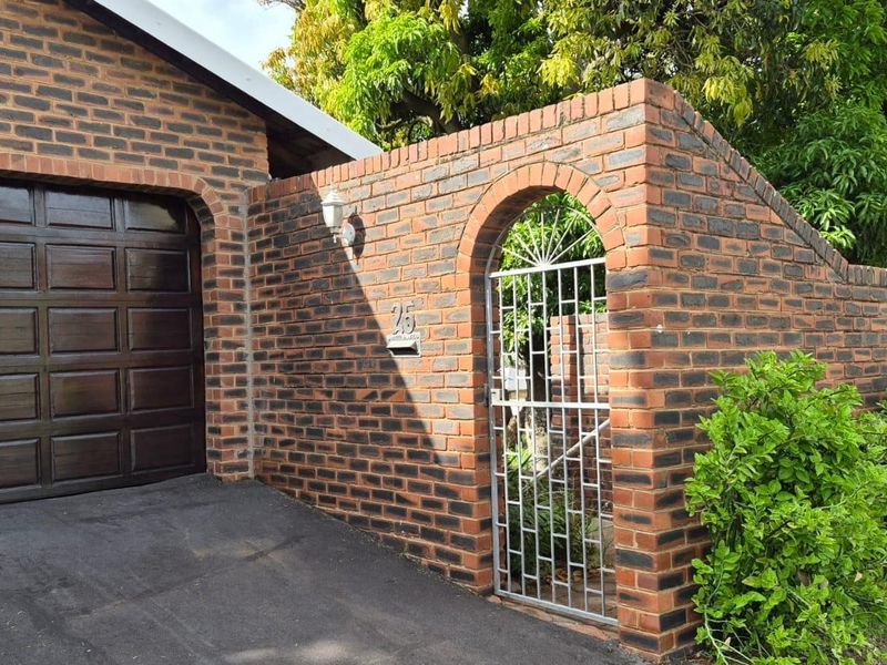 Front exterior view featuring a face brick facade, arched pedestrian gate, and a secure sectional garage door with an asphalt driveway.