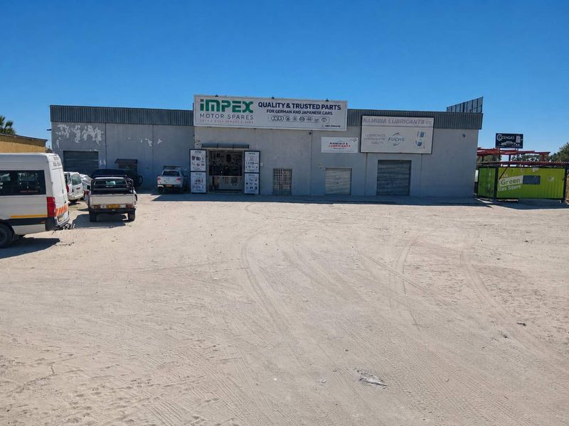 Front elevation of a commercial motor spares facility featuring roller shutter doors, metal cladding, and prominent business signage on a large gravel lot.