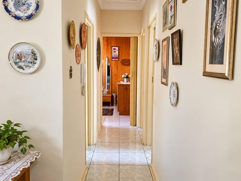 A well-lit residential hallway featuring neutral wall tones and tiled flooring, providing access to multiple rooms within the retirement village unit.