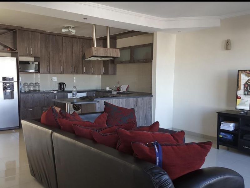 Open-plan living area featuring a modern kitchen with wood-finish cabinetry, integrated appliances, and tiled flooring, seamlessly flowing into the lounge space.
