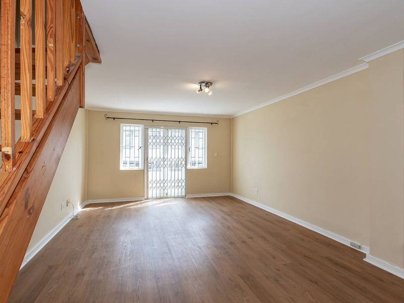 Spacious, light-filled living area featuring modern laminate flooring, a wooden staircase, and a secure sliding door leading to the exterior.