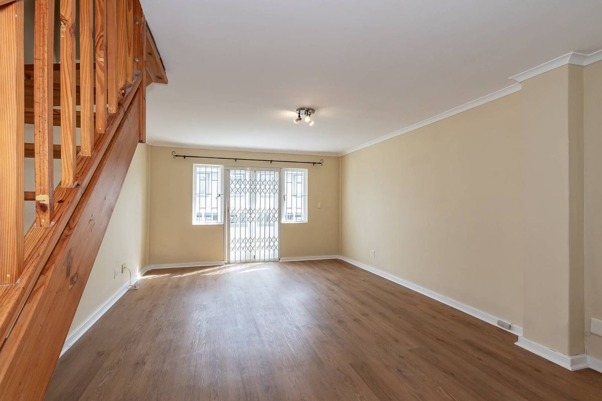Spacious, light-filled living area featuring modern laminate flooring, a wooden staircase, and a secure sliding door leading to the exterior.
