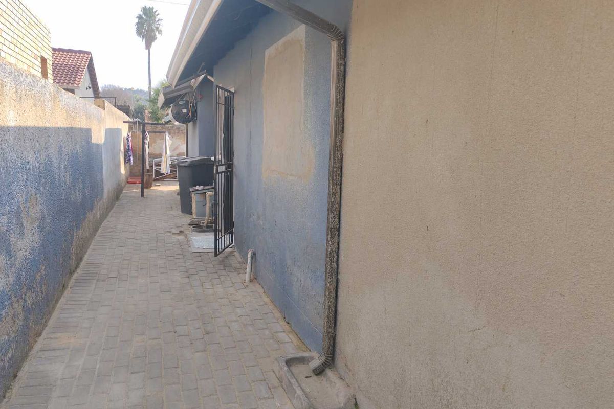 A narrow paved side passage along the exterior of the house featuring a downpipe and security gate access.