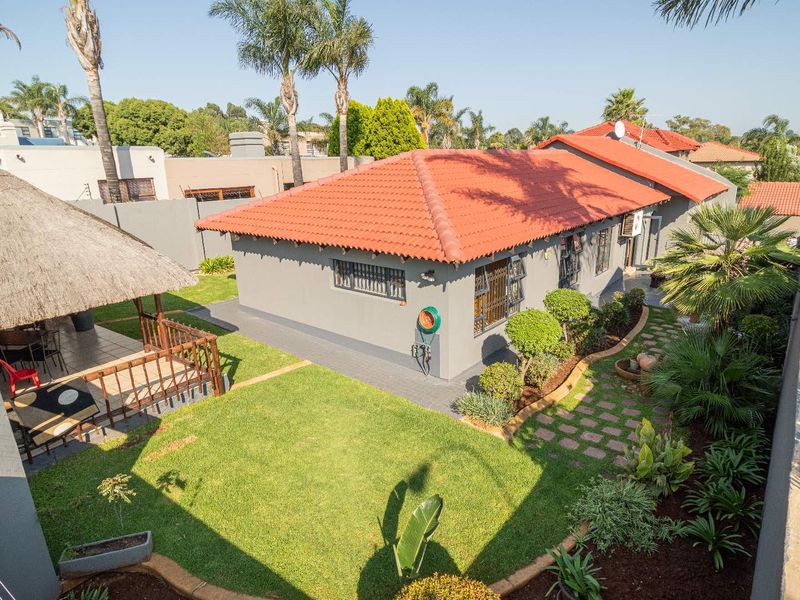 Aerial view of the rear garden featuring a thatched lapa, paved pathways, and well-maintained landscaping surrounding the cluster home.