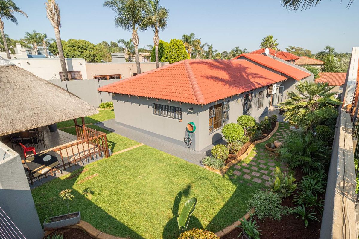 Aerial view of the rear garden featuring a thatched lapa, paved pathways, and well-maintained landscaping surrounding the cluster home.