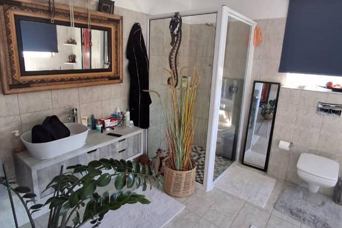 A modern bathroom featuring a wall-mounted toilet, a glass-enclosed shower, and a vanity with a vessel sink, finished with neutral wall and floor tiles.