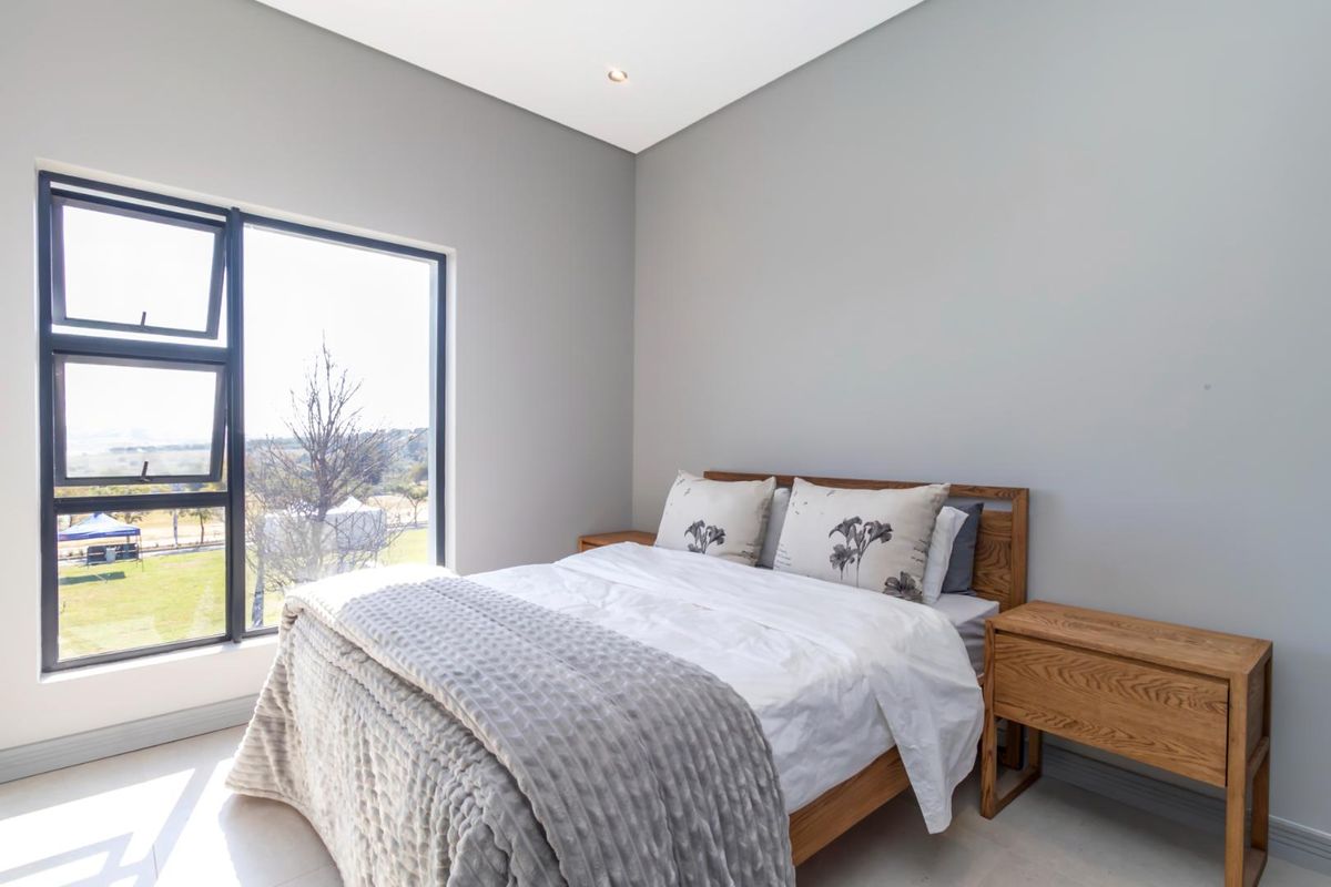 A bright and modern bedroom featuring large aluminium-framed windows, neutral wall finishes, and recessed ceiling lighting.