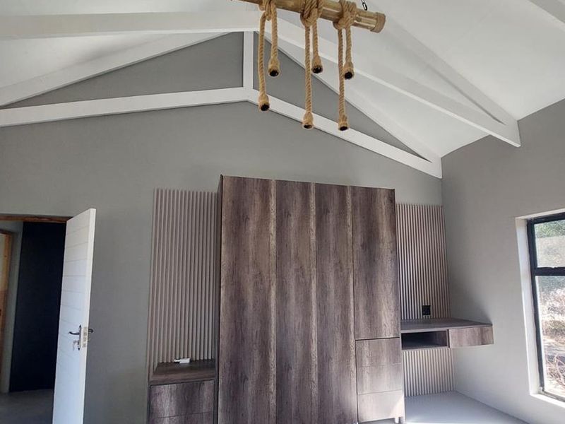 Modern bedroom featuring a high vaulted ceiling with exposed rafters, built-in wood-finish cabinetry, integrated desk space, and sleek slatted wall detailing.