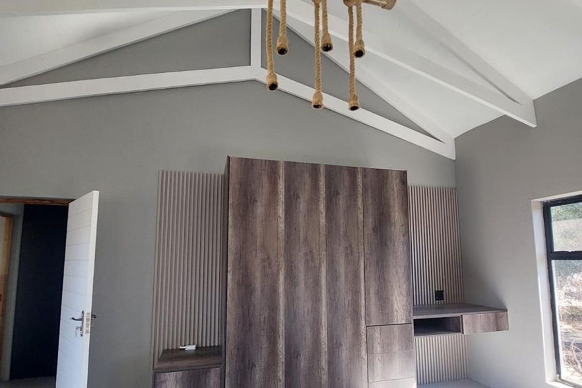 Modern bedroom featuring a high vaulted ceiling with exposed rafters, built-in wood-finish cabinetry, integrated desk space, and sleek slatted wall detailing.