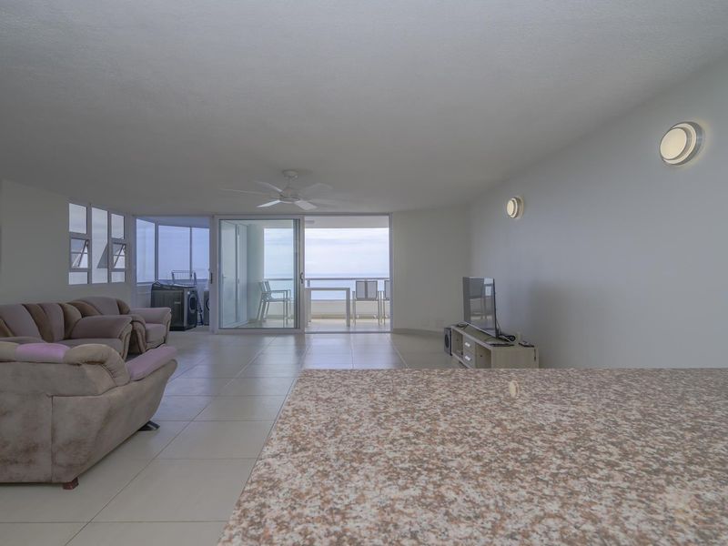 Spacious open-plan living area featuring tiled flooring, a granite breakfast bar, and sliding glass doors leading to a balcony with ocean views.