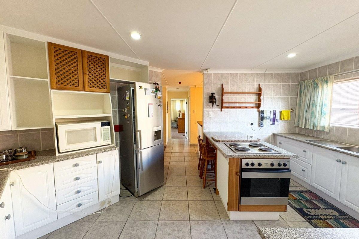 A functional kitchen featuring white cabinetry, granite countertops, a built-in oven with hob, and tiled flooring, leading into a central hallway.