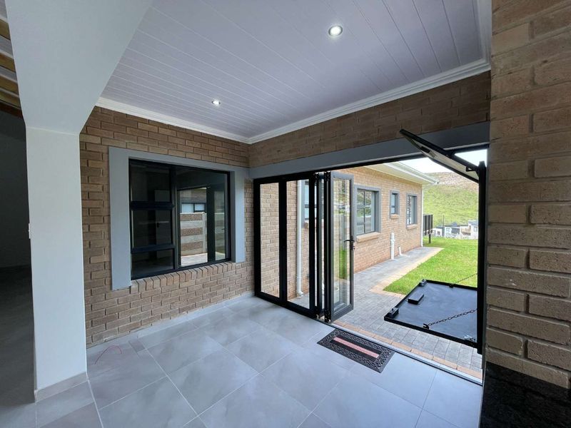A modern covered patio featuring exposed brick walls, tiled flooring, and bi-fold doors that open to the rear garden area.