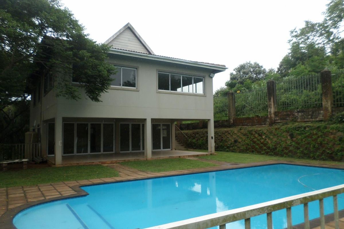 Rear view of a two-story house featuring a swimming pool, covered patio area, and landscaped garden with retaining wall.