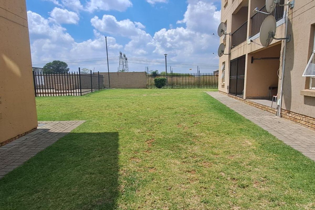 A communal garden area between townhouse blocks featuring paved walkways, manicured lawn, and perimeter steel fencing.