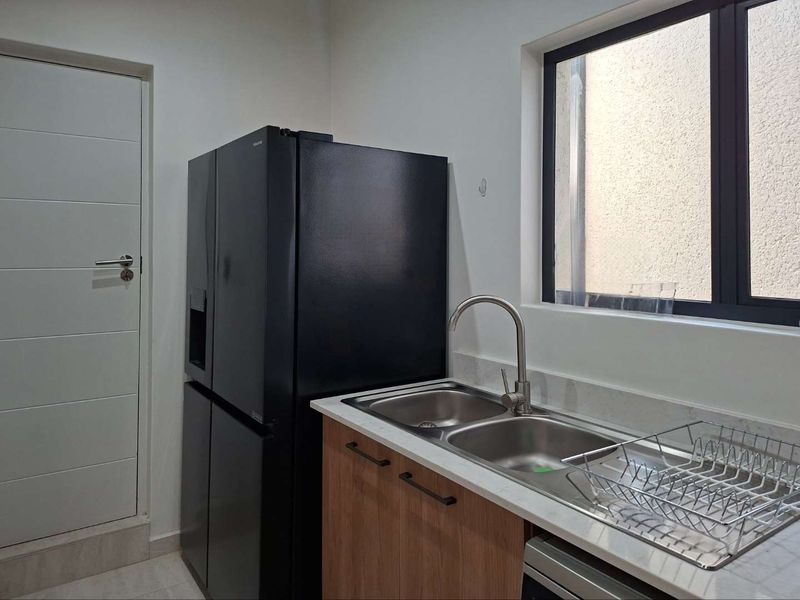 A functional scullery area featuring a double bowl stainless steel sink, stone countertops, modern cabinetry, and a window providing natural light.