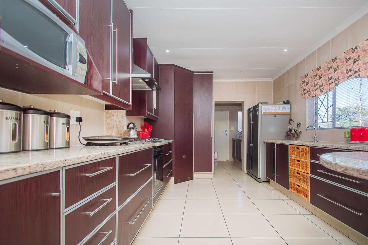 A functional kitchen featuring dark wood cabinetry, granite countertops, tiled flooring, and integrated appliances, with an adjacent scullery area.
