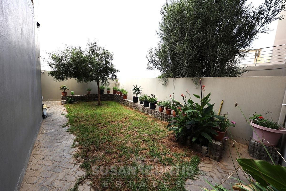 A private rear garden featuring a paved walkway, a small lawn area, and perimeter boundary walls with raised planter beds.
