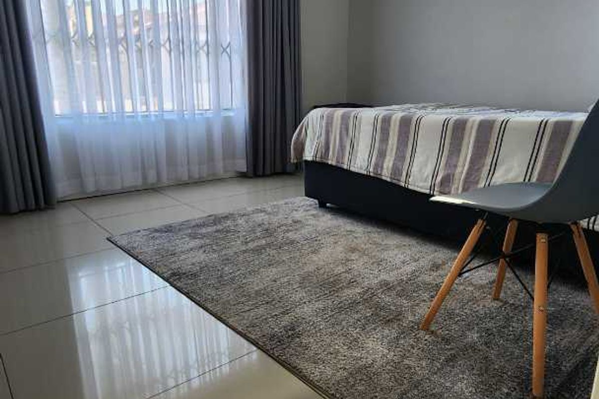 A bright bedroom featuring large windows with security gates, neutral wall finishes, and polished floor tiles.