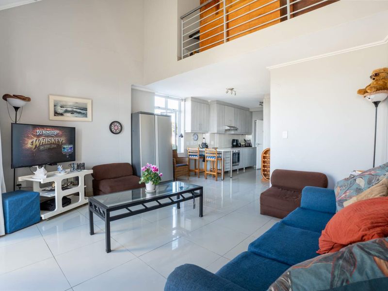 Open-plan living area featuring high ceilings, a mezzanine level with metal balustrade, and a functional kitchen with built-in cabinetry and appliances.