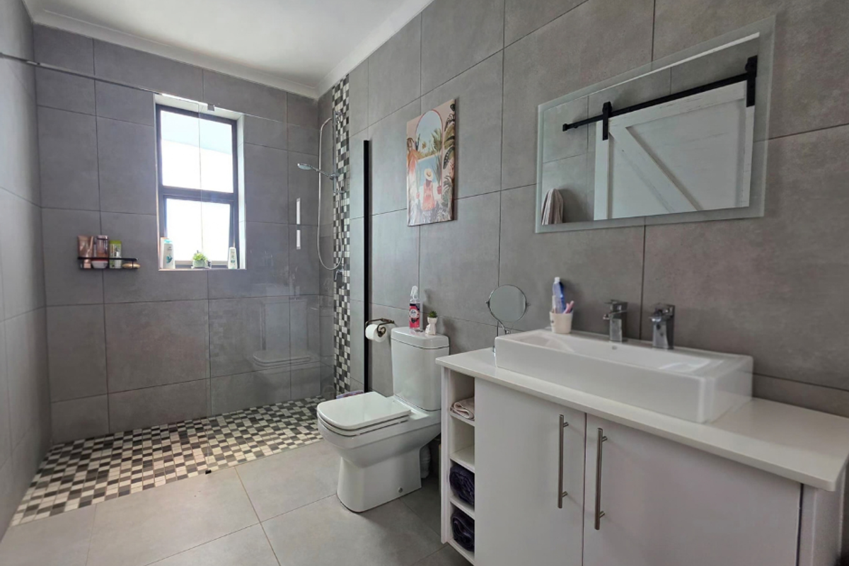 Modern bathroom featuring large format grey wall tiles, a walk-in shower with mosaic accents, a white vanity with countertop basin, and a wall-mounted mirror.