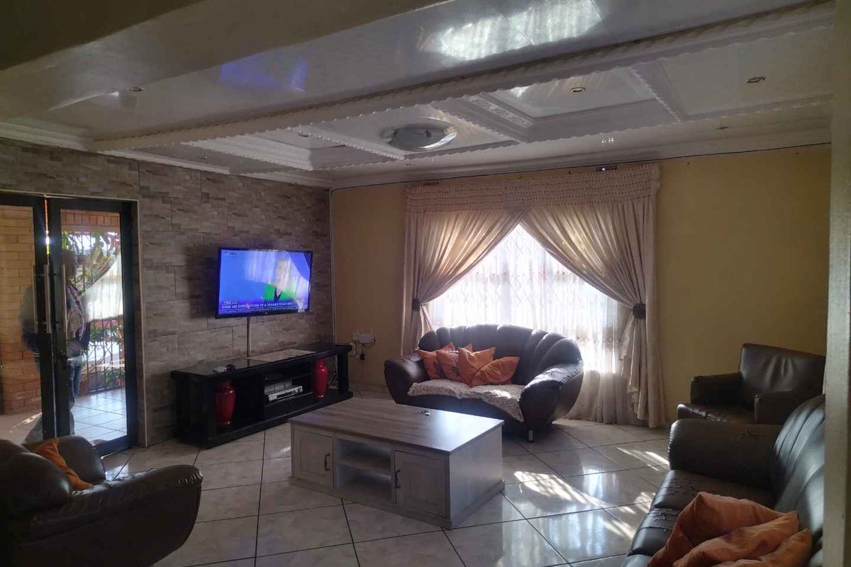 A spacious living room featuring tiled flooring, a decorative ceiling, and a stone-cladding feature wall, providing a comfortable and functional family living space.