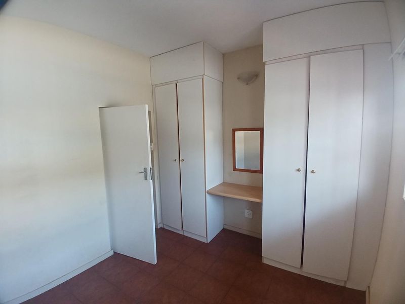 A clean, empty bedroom featuring built-in white cupboards, a small integrated vanity area, and tiled flooring.