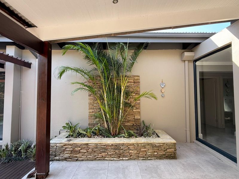 A well-maintained covered patio featuring a stone-clad planter box, timber pergola structure, and large sliding glass doors providing access to the interior.