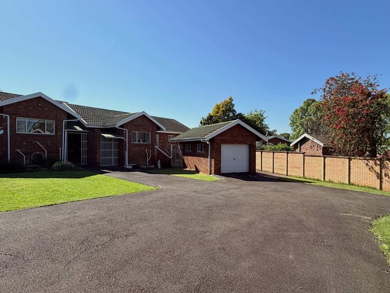 Front exterior view of a brick townhouse featuring a tiled roof, a single garage, and a paved driveway with a surrounding brick boundary wall.