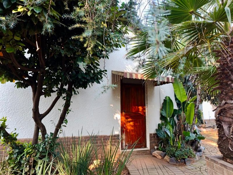 A rear exterior view of the cottage featuring a wooden door with a small awning, set against a textured wall and surrounded by garden foliage.