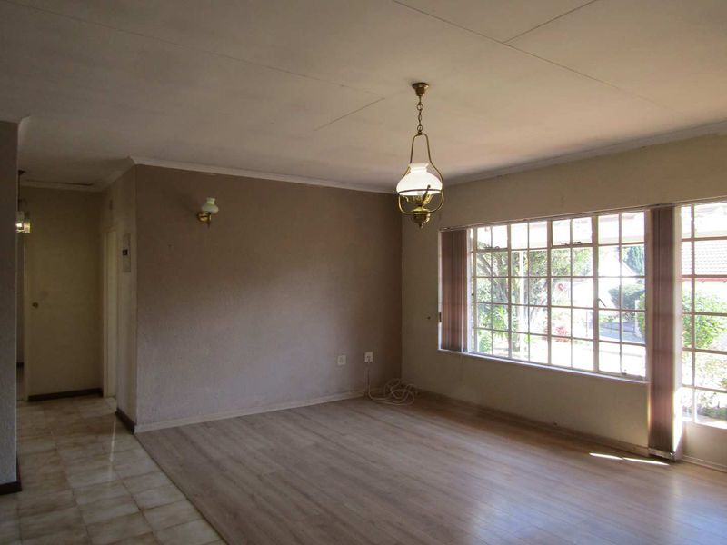 An empty, sunlit living room featuring a combination of laminate and tiled flooring, large windows, and classic lighting fixtures.