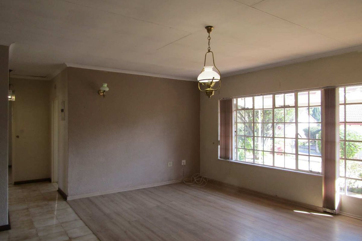 An empty, sunlit living room featuring a combination of laminate and tiled flooring, large windows, and classic lighting fixtures.
