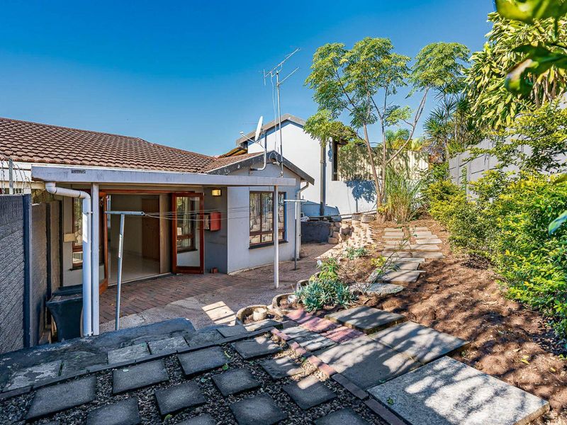 Rear exterior view of the townhouse featuring a covered patio, paved garden pathways, and perimeter boundary walls with security fencing.