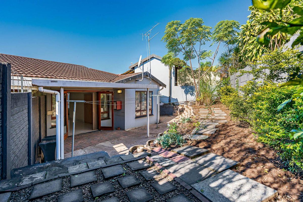 Rear exterior view of the townhouse featuring a covered patio, paved garden pathways, and perimeter boundary walls with security fencing.