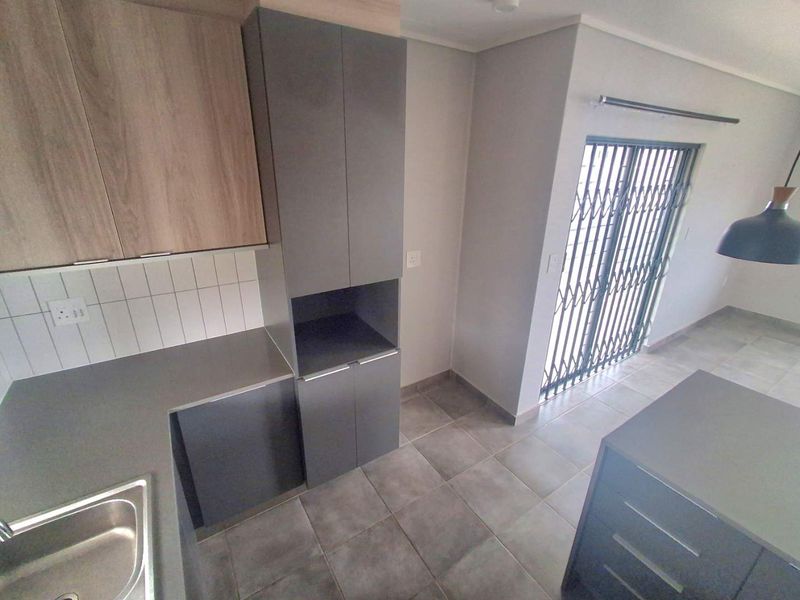 Modern kitchen featuring sleek grey and wood-tone cabinetry, tiled backsplash, stainless steel sink, and direct access to an outdoor area via a security gate.
